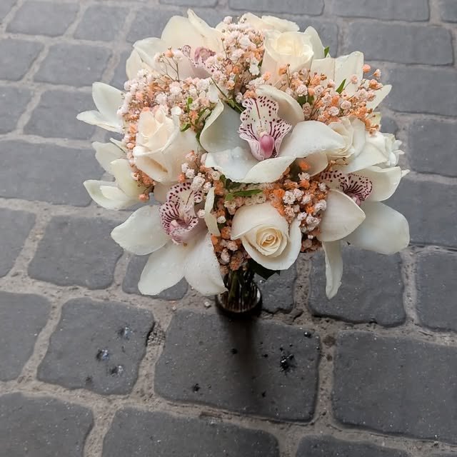 Ramo de rosas blancas, calas y orquídeas rosadas sobre adoquín